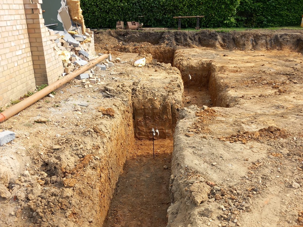 A foundation footing trench dug alongside part-demolished brickwork